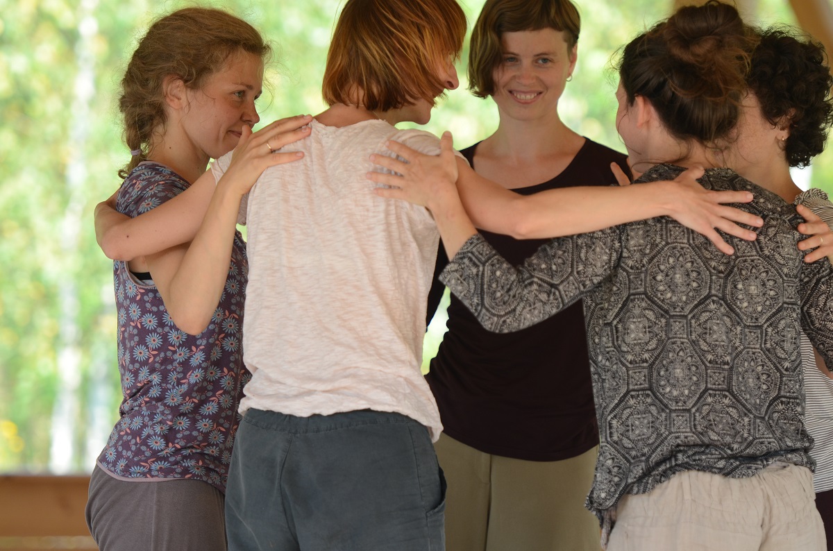 5 women standing in a small circle with their arms around one another